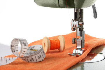 Sewing machine with orange fabric, measuring tape and spool of thread isolated on white