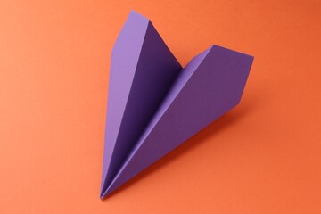 One handmade violet paper plane on orange background, closeup