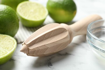 Wooden juicer and fresh limes on white marble table, closeup