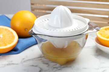 Plastic juicer and fresh oranges on white marble table, closeup
