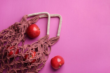 Handmade macrame shopping bag with apples on crimson background, top view. Space for text