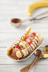 Delicious sweet banana split ice cream dessert with berries syrup or topping and cherry.