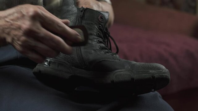 Elderly woman cleaning black shoe while sitting on sofa.Hands and boot close-up.