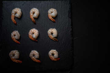 Boiled, frozen shrimp on a black mica board, laid out in rows. Place for text.