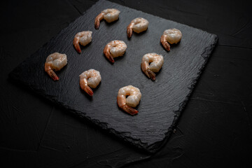 Boiled, frozen shrimp on a black mica board, laid out in rows. Place for text.