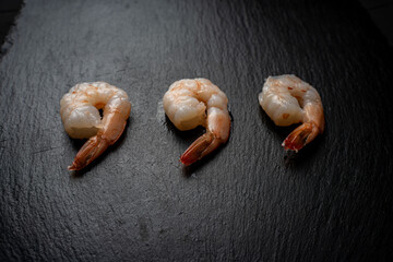 Three boiled, frozen shrimp on a black mica board, laid out in a row. Place for text.