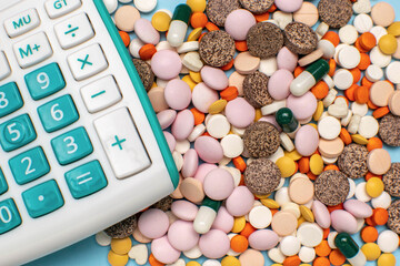 Colorful Assortment of Pills and Capsules with Calculator on Blue Surface Reflecting Healthcare...