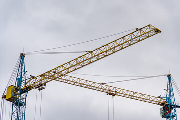 Massive construction cranes stretch towards the overcast sky, showcasing their intricate structure. They are pivotal in shaping the evolving city landscape, highlighting industrial progress