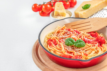 Spaghetti in tomato sauce with cheese in red pan on a light background. copy space