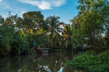 Obraz premium Palm trees, boats and buildings reflecting on the quiet waters of the canals in Can Tho in Vietnam