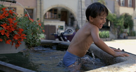 Young boy happily playing in a stone fountain, splashing water while smiling and enjoying the fun...