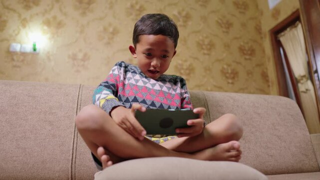 Close-up of a boy playing smart phone games at home with a competitive expression. The intensity and focus reflect the excitement of playing the game
