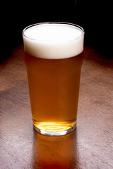 pint of craft pale ale beer in close-up seen from angle on wooden table, foam and dark background
