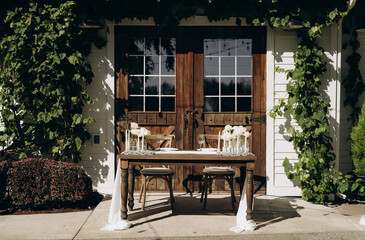 Romantic wedding table for two with white flowers and candles on the background of a wooden door...