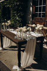 Outdoor celebration table with white roses, candles and classic white textiles.