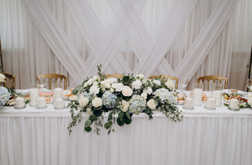 White wedding presidium with drapery, hydrangeas, roses and candles on the background of geometric textiles.