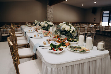 Wedding banquet: white draped table with light snacks, golden chiavari chairs and flower...