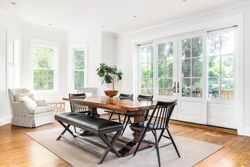 A cozy dining room with a large wooden table and chairs on an area rug and hardwood floor.