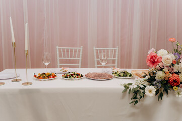 White bridal table with flowers and candles on a pink background.