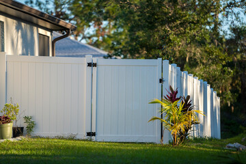 White vinyl picket fence on green lawn surrounding property grounds for backyard protection and...