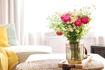 Beautiful ranunculus flowers and chamomiles in vase on table indoors