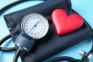 Blood pressure measuring device and heart figure on light blue background, closeup
