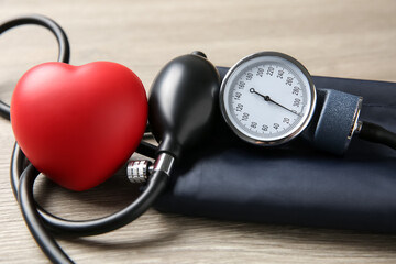 Blood pressure measuring device and squeeze heart on wooden table, closeup