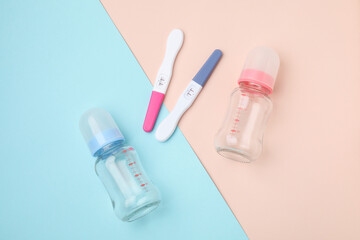 Two pregnancy tests and baby bottles on color background, flat lay