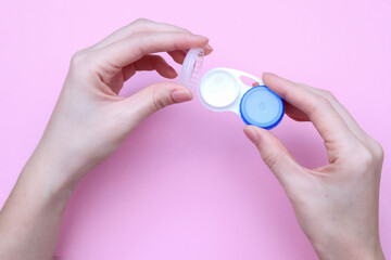 Hands holding contact lens, on a pink background, closeup. 