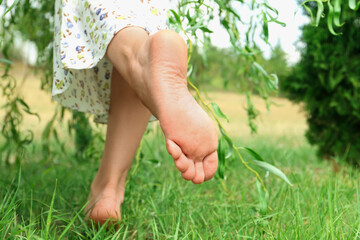 Woman walking barefoot on green grass outdoors, closeup
