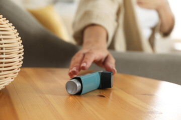 Woman reaching for asthma inhaler at wooden table indoors, closeup