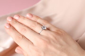Woman wearing beautiful ring with gemstone against beige fabric, closeup