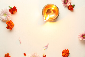 Diwali celebration. Diya lamp and beautiful flowers on light textured surface, flat lay. Space for text
