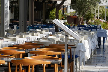 Empty utdoor restaurant with a menu stand in foreground for passers by. The tables are decorated in blue and white and are captured in diminishing perspective. 