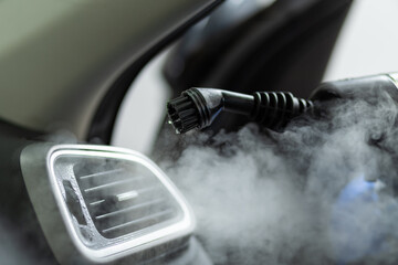 A steam cleaner nozzle is pointed at the air vent of a car during a detail