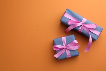 Beautiful gift boxes with pink bows on orange background, top view. Space for text