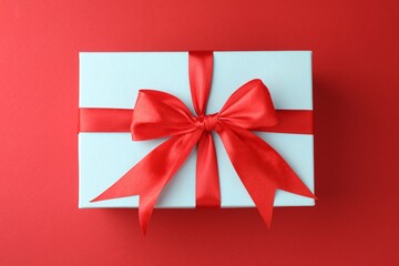Gift box with bow on red background, top view