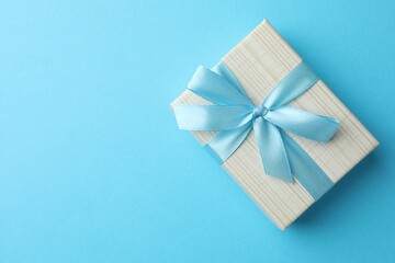 Gift box with bow on light blue background, top view. Space for text