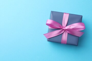 Gift box with bow on light blue background, top view. Space for text