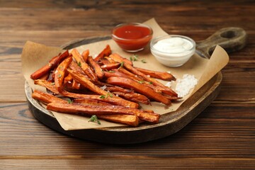 Delicious sweet potato fries with sauces and spices on wooden table, closeup