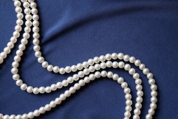 Elegant pearl necklace on dark blue fabric, top view