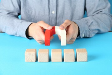 Man with magnet attracting wooden cubes on light blue background, closeup