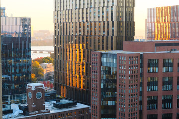 Golden hour light reflects off tall business buildings in Cambridge city, creating a warm glow that...