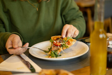 A woman holds a piece of pizza in hands. Focus on a pizza. Pizza with prosciutto, ham, arugula, tomatoes and parmesan. Italian cuisine. Food banner