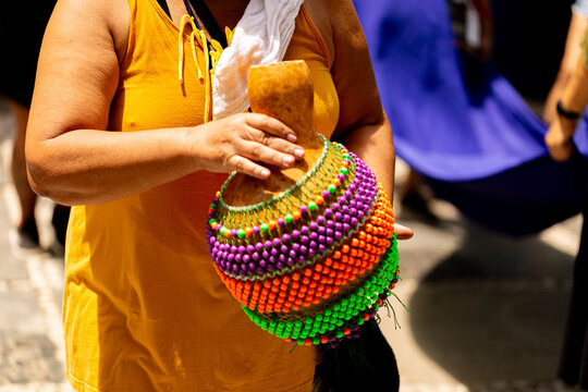 Afox&eacute; &eacute; um instrumento musical composto de uma caba&ccedil;a pequena redonda, recoberta com uma rede de bolinhas de pl&aacute;stico. Mulher tocando Afox&eacute; em bloco de carnaval de rua. 