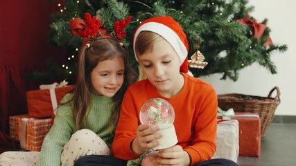 A group of children delight in the magical wonders of a snow globe as they gather joyfully beneath the beautifully decorated Christmas tree