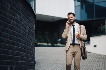 Businessman walking and talking on phone outside office building - Powered by Adobe