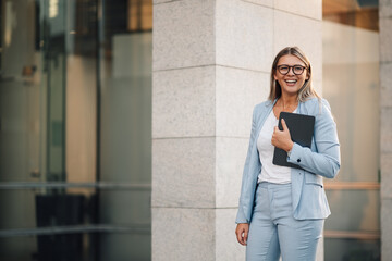 Businesswoman smiling holding digital tablet outside office building