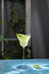 Yellow cocktail decorated with basil leaves on a blue table