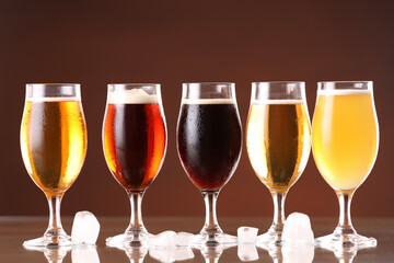Glasses with different types of beer and ice cubes on mirror surface